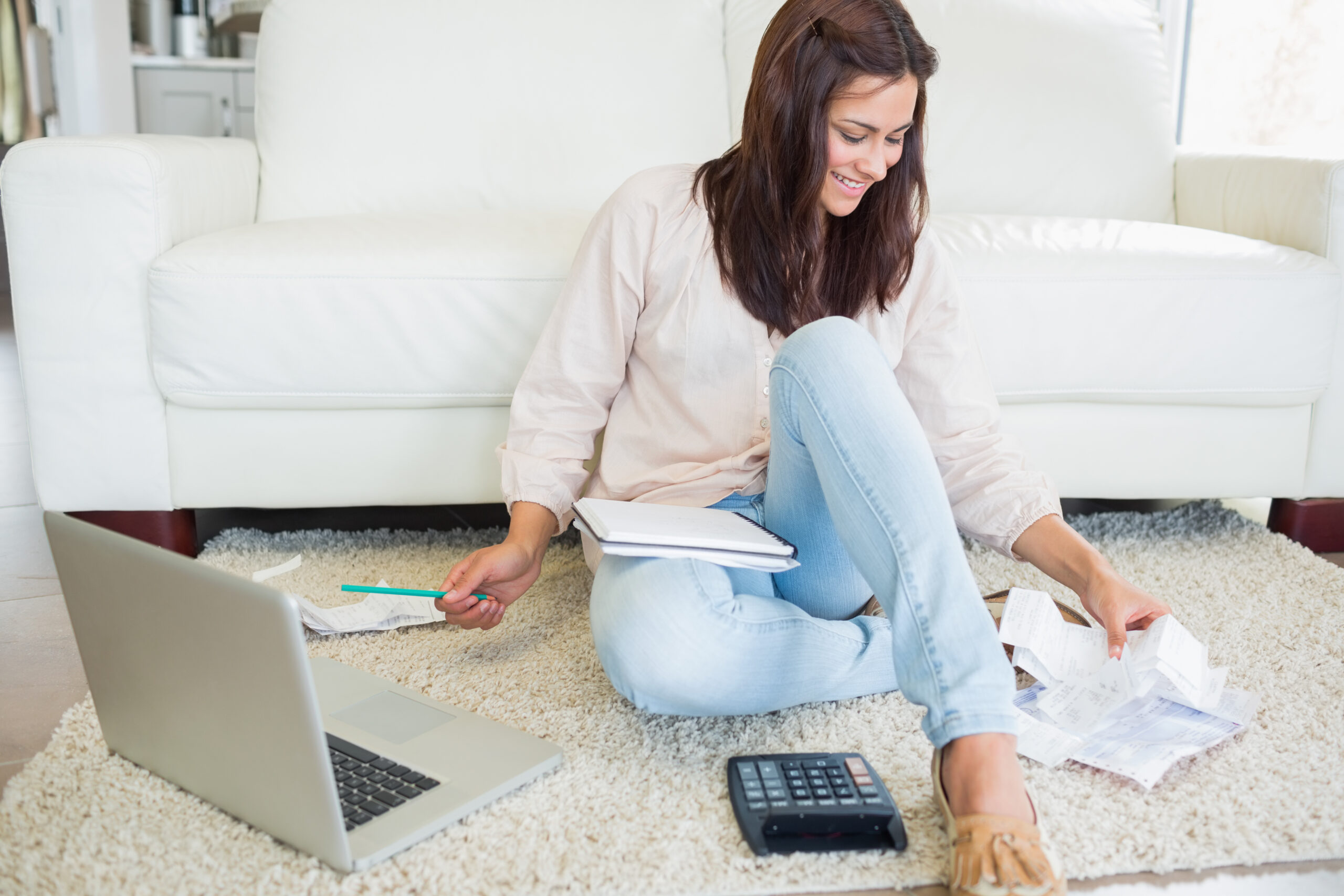 Woman using laptop to calculate bills on floor of living room