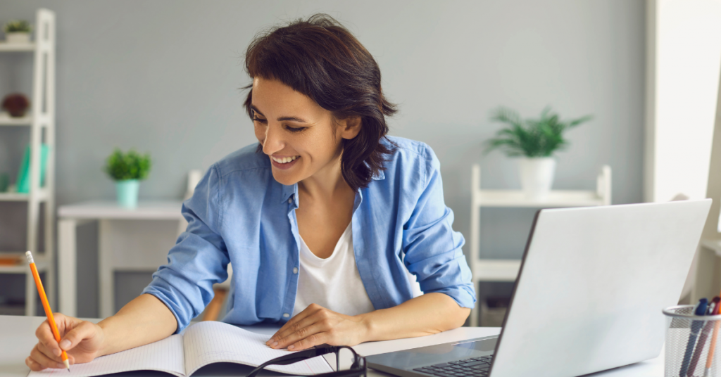 woman writing in notebook with laptop